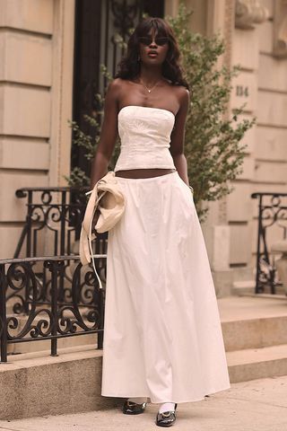 a photo of a woman wearing a white maxi skirt outfit with a white tube top and black ballet flats