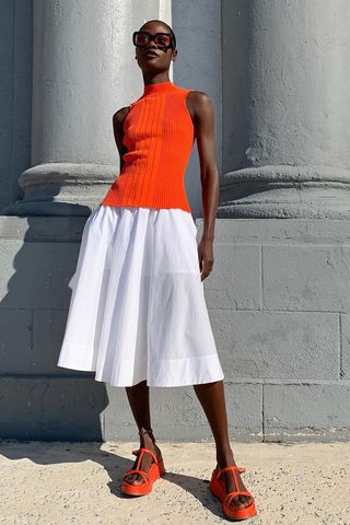 a photo of a woman wearing a full white skirt outfit with an orange top and orange sandals