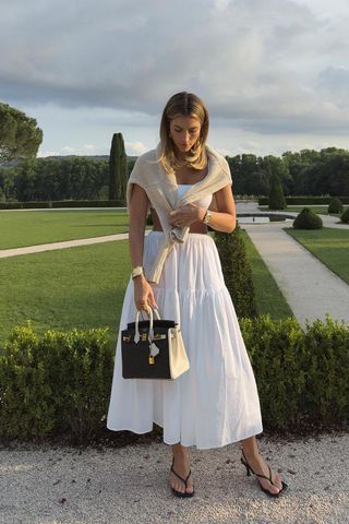 a photo of a woman wearing a white midi skirt with white tank and cardigan and black sandals