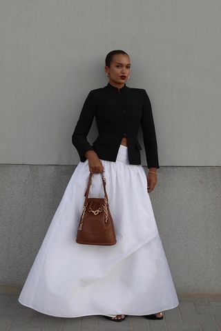 a woman wearing a white maxi skirt outfit with black blazer and black flat sandals