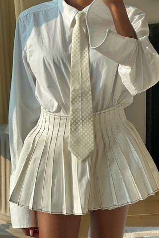 a close photo of a woman wearing a white pleated mini skirt with a white button-down shirt and matching men's tie