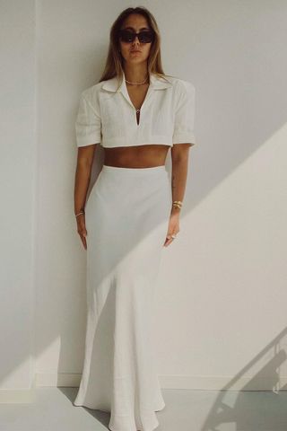 a photo of a woman wearing a white maxi skirt with a cropped white polo shirt and big sunglasses