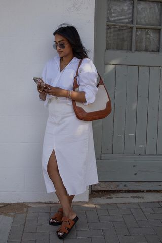 a woman wearing a white denim skirt outfit with a button-down shirt, brown bag, and brown sandals