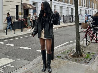 Woman wearing a black leather jacket, a miniskirt, and knee-high boots.