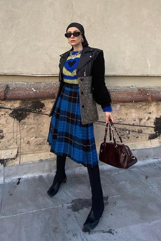 a woman's skirt outfit with a plaid mini skirt and a printed sweater and leggings and ankle boots
