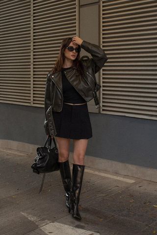 a woman's skirt outfit with a black mini skirt styled with a leather motocycle jacket and whit t-shirt and black knee high boots