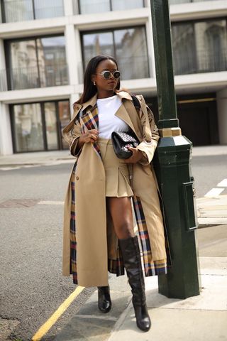 a woman's skirt outfit with tan cargo mini styled with a white t-shirt and trench coat and knee-high boots