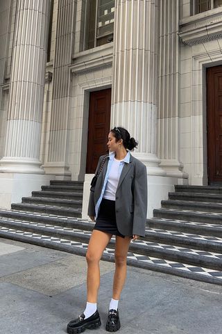 a woman's skirt outfit with a black mini skirt styled with a t-shirt, button-down shirt, and gray blazer and black loafers