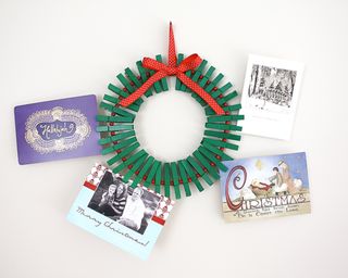 A christmas card wreath made from green spray painted pegs, red beads and printed red and white ribbon