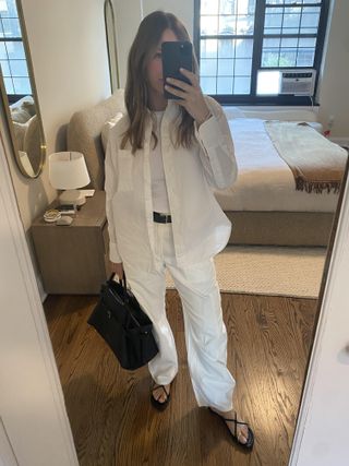 Nikki Chwatt wearing the white Marcelle cargo pants, a white button down, a black belt, black sandals, and a black handbag,