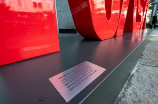 a silver plaque with sits on a dark-gray metallic surface that supports a red sculpture that reads "nasa" in the famous "worm" font.