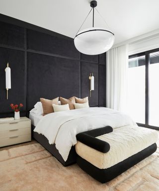 A white bed with brown and white pillows against a black accent wall.