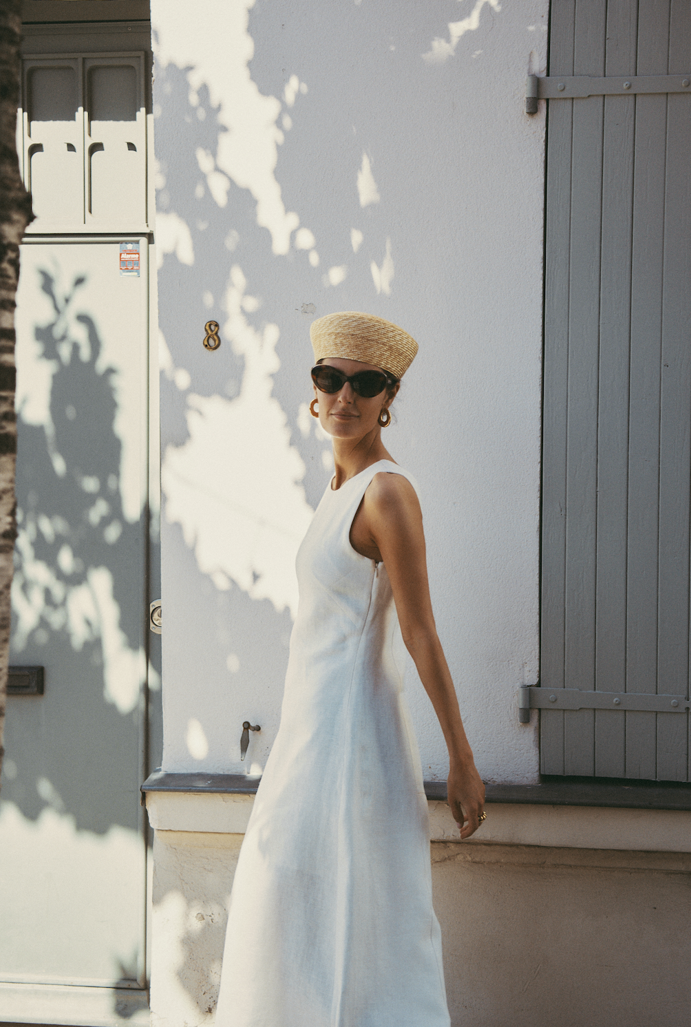 Maria de la Orden wears white dress, black sunglasses, straw hat and hoop earrings in the sun