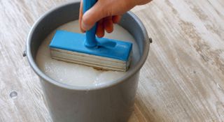 Man dipping wallpapering brush into a bucket of wallpaper paste