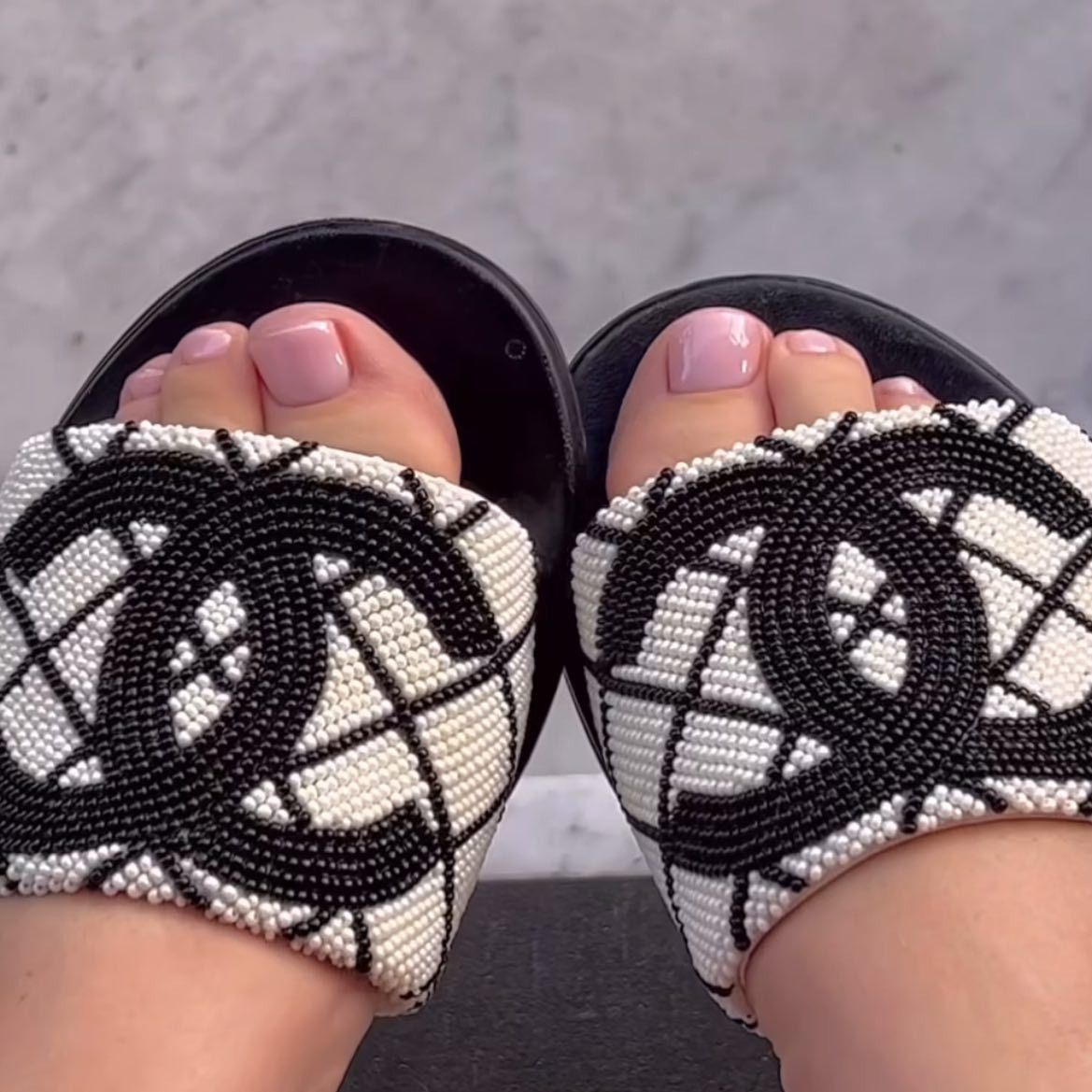 A woman wearing black and white Chanel sandals with a soft pink pedicure