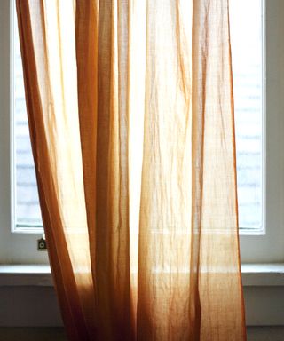 White window that's closed with an orange curtain in front of it