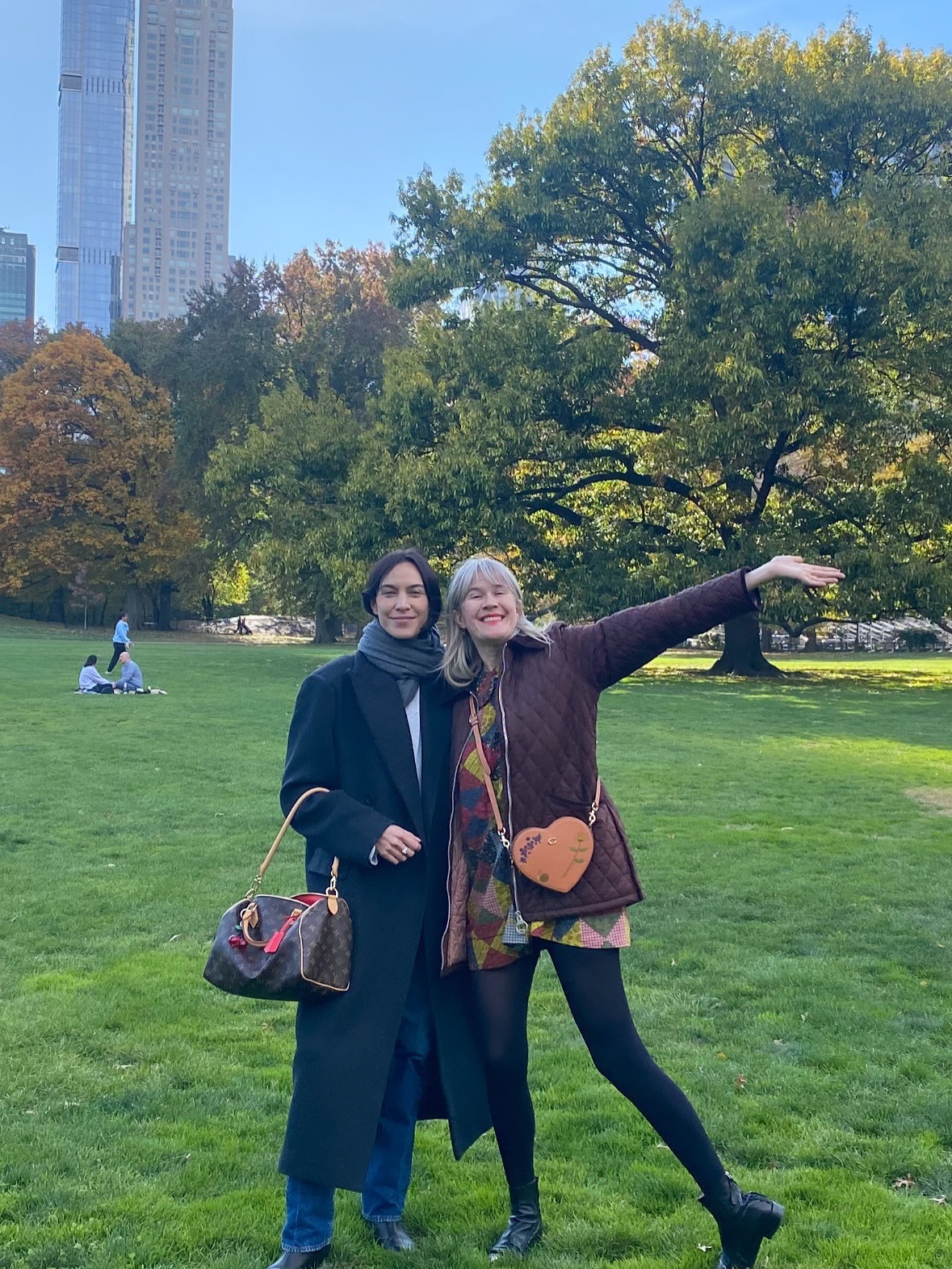 Alexa Chung stands in Central Park wearing a Louise Vuitton Speedy bag with a black wool coat.
