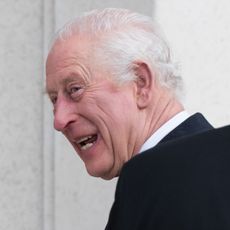 A headshot of King Charles smiling and turning dto the side wearing a black coat 