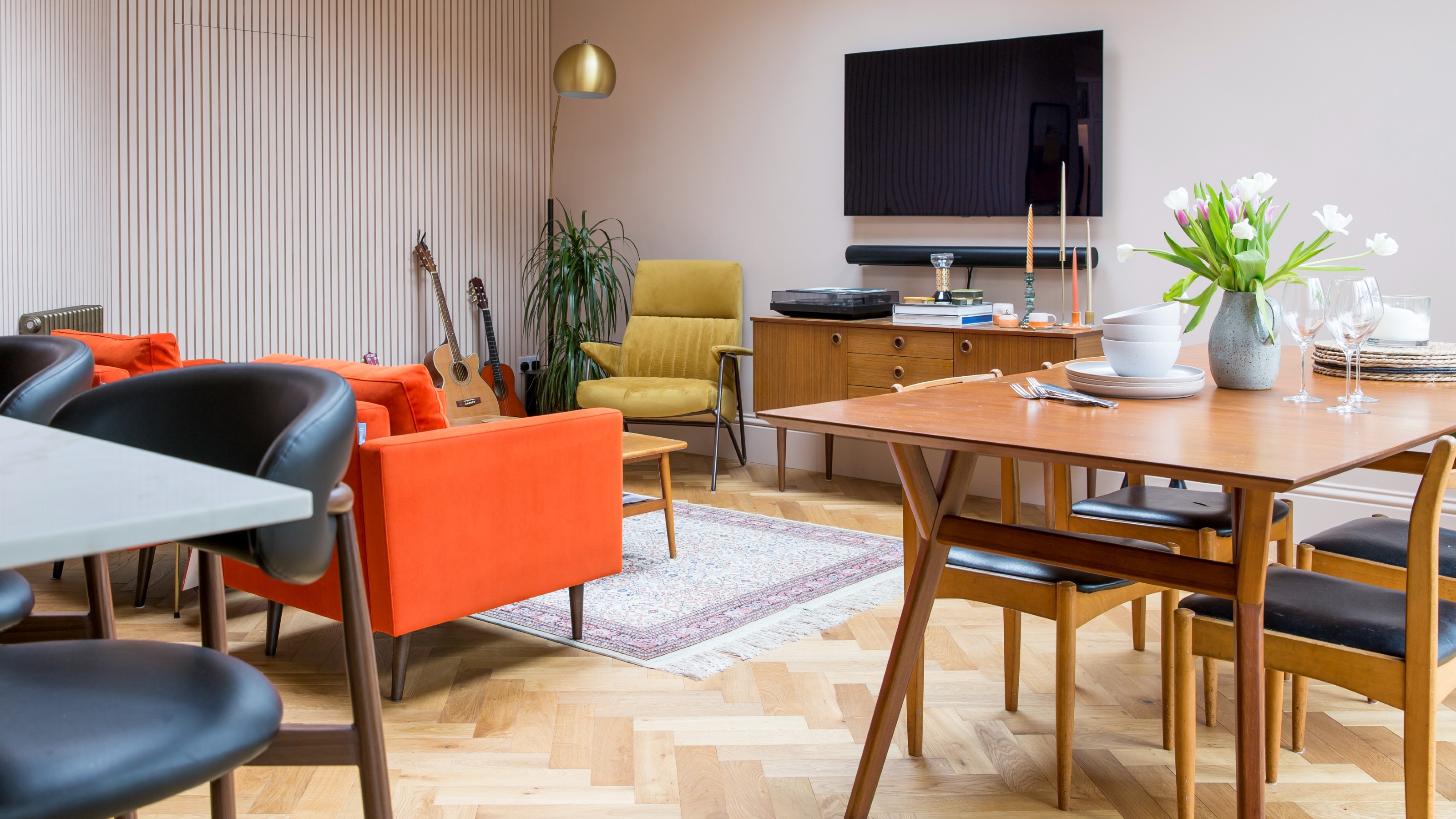 A living room with a panelled wall, an orange sofa and a dining area