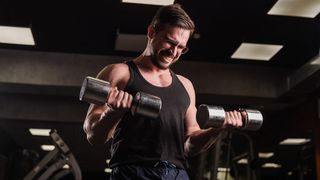 Man strains while performing biceps curls with dumbbells