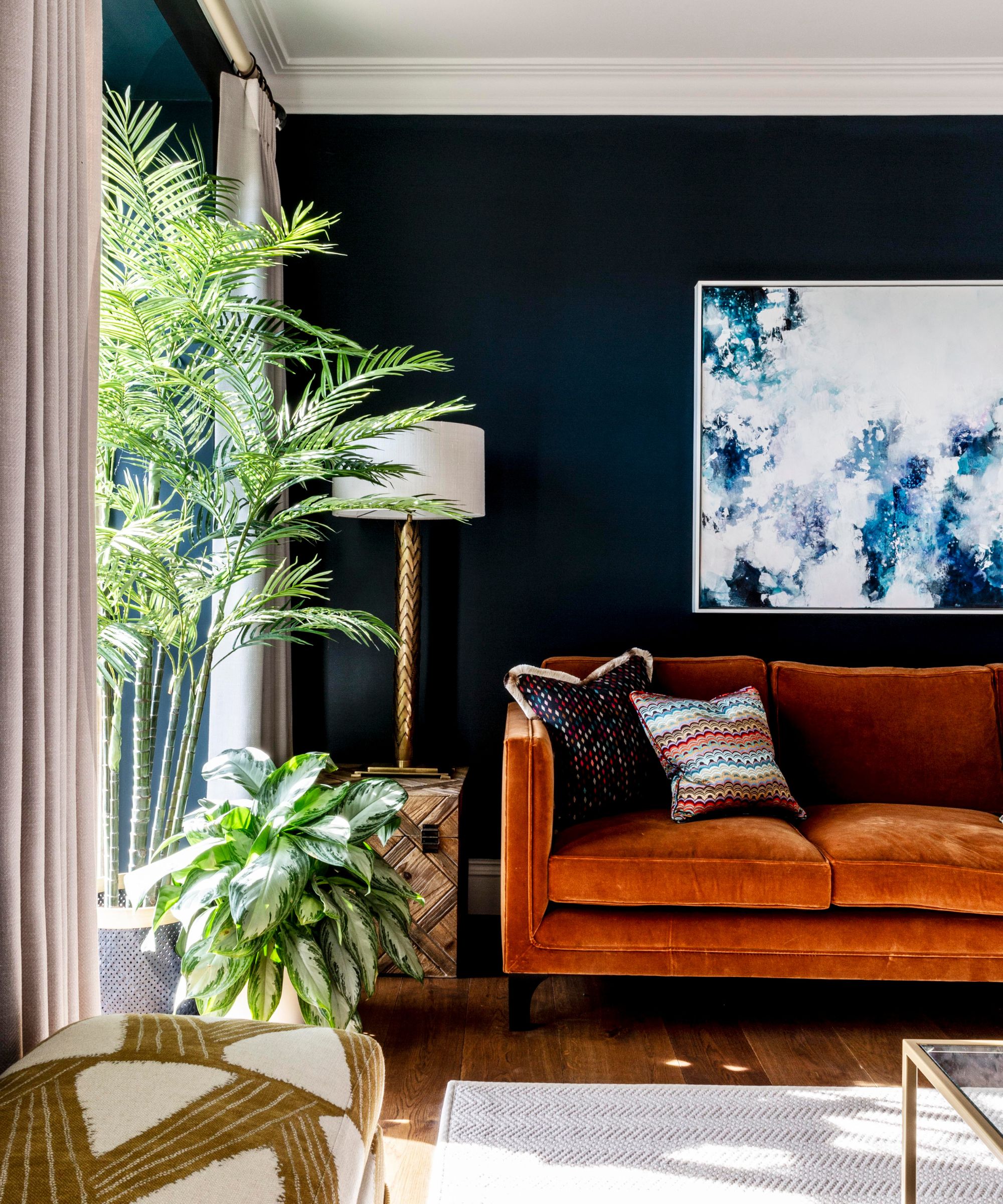 Wide view of the same navy room showing two large artworks &amp;mdash; an abstract blue canvas and a painted portrait &amp;mdash; flanking a floor-to-ceiling window with linen curtains and tropical plants.