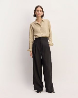 a model wears a light brown button-down shirt with black wide-leg trousers