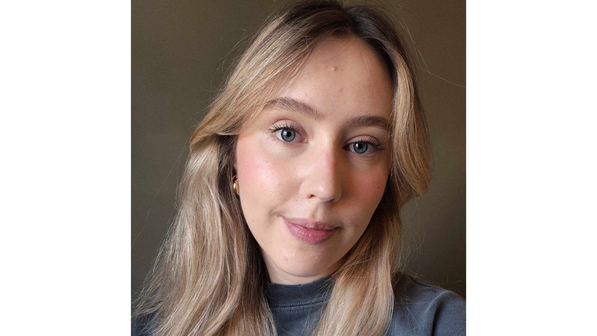 Naomi smiling with long blonde hair and wearing the Merit Uniform Tinted SPF