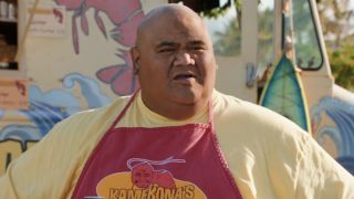 Taylor Wily's Kamekona sitting at bench outside food drunk wearing apron in Hawaii Five-0 Season 10 premiere