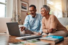 A couple sitting on a couch reviewing their savings on a laptop