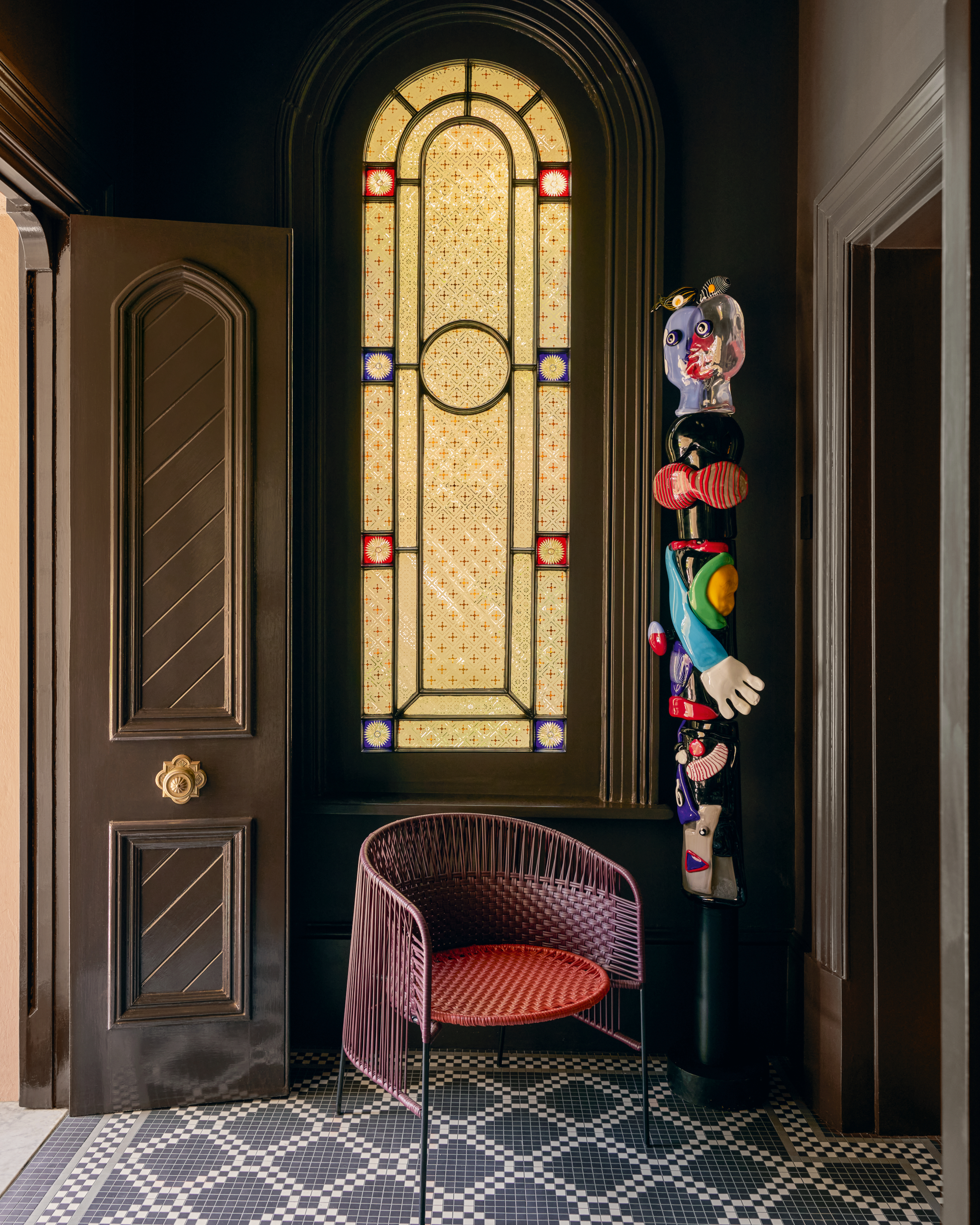 Entrance vestibule with stained glass window, pink and red tope chair and totem sculpture