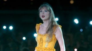 Taylor Swift singing "Marjorie" in a yellow dress with cell phone lights shining in the background