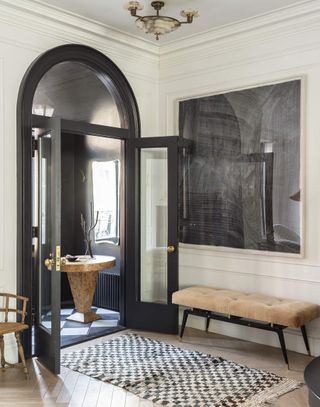 Hallway with large black arch over the glass front door, pale wood flooring and black and white rug.
