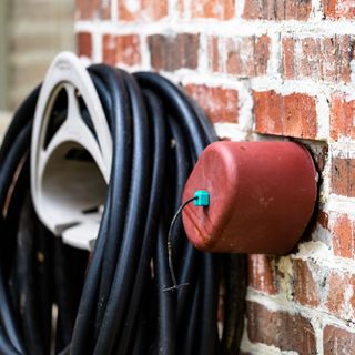 Garden tap on an exterior brick wall with an insulating cover on it, next to a garden hose