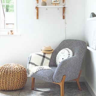 Grey boucle armchair with wooden legs, with white blanket and cushion beneath wooden shelves