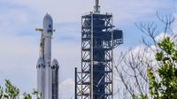 A triple core rocket with one sooty booster stands at a launch pad.