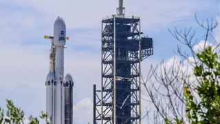 A triple core rocket with one sooty booster stands at a launch pad.