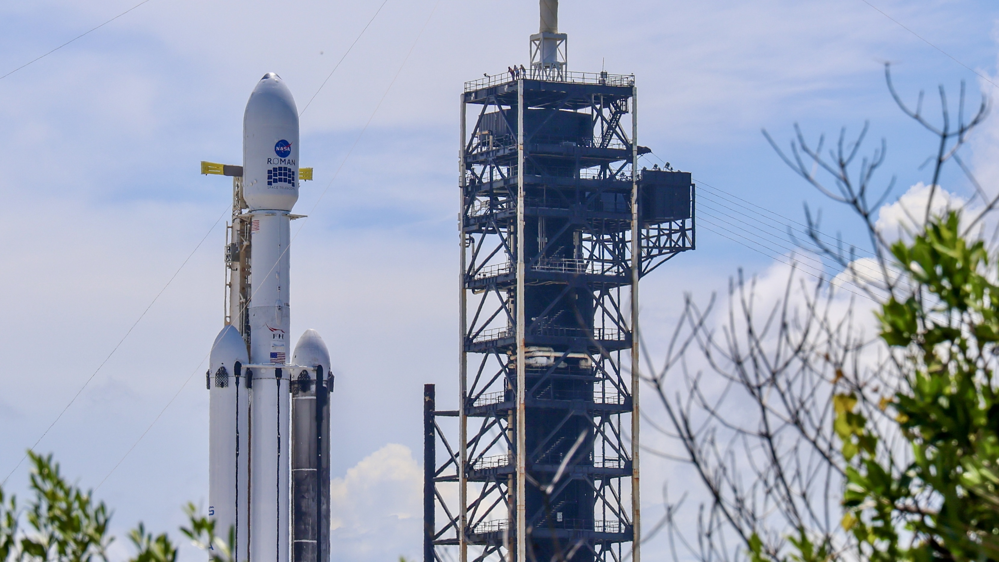 A triple core rocket with one sooty booster stands at a launch pad.