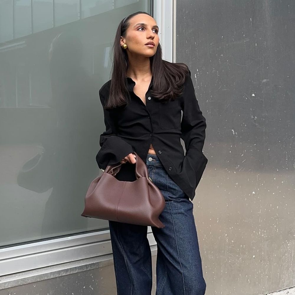 @ingridedvinsen wearing dark-blue pintuck jeans with a black fitted button-down shirt and dark brown leather tote