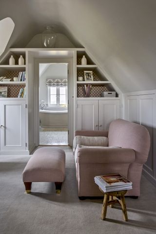 Armchair and footstool with built in shelves and cupboards in neutral room with sloping ceiling