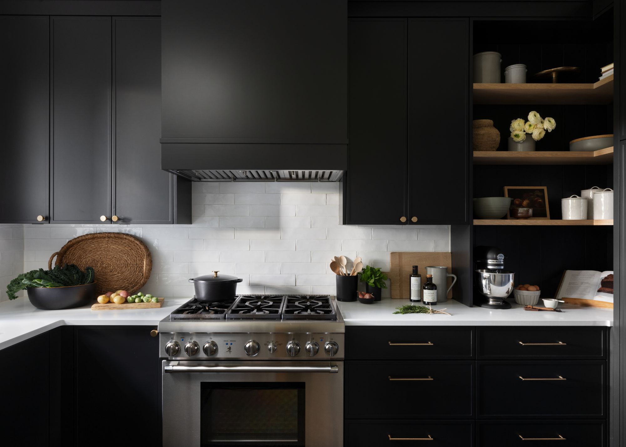An all-black kitchen with white backsplash, and wooden cutlery