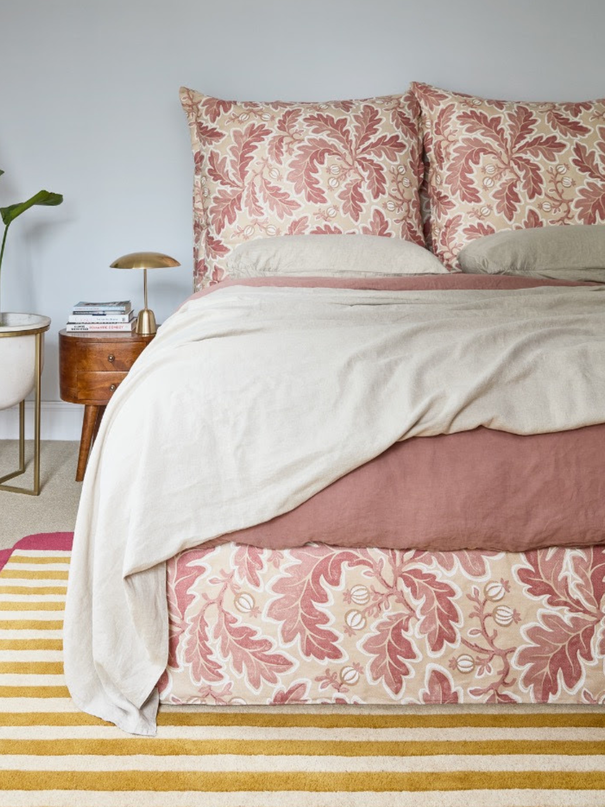 orange bed with leaf print pattern on the cushions and frame in grey bedroom with stripy rug