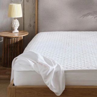 A white quilted mattress protector on a mattress in a bedroom with a wooden bed