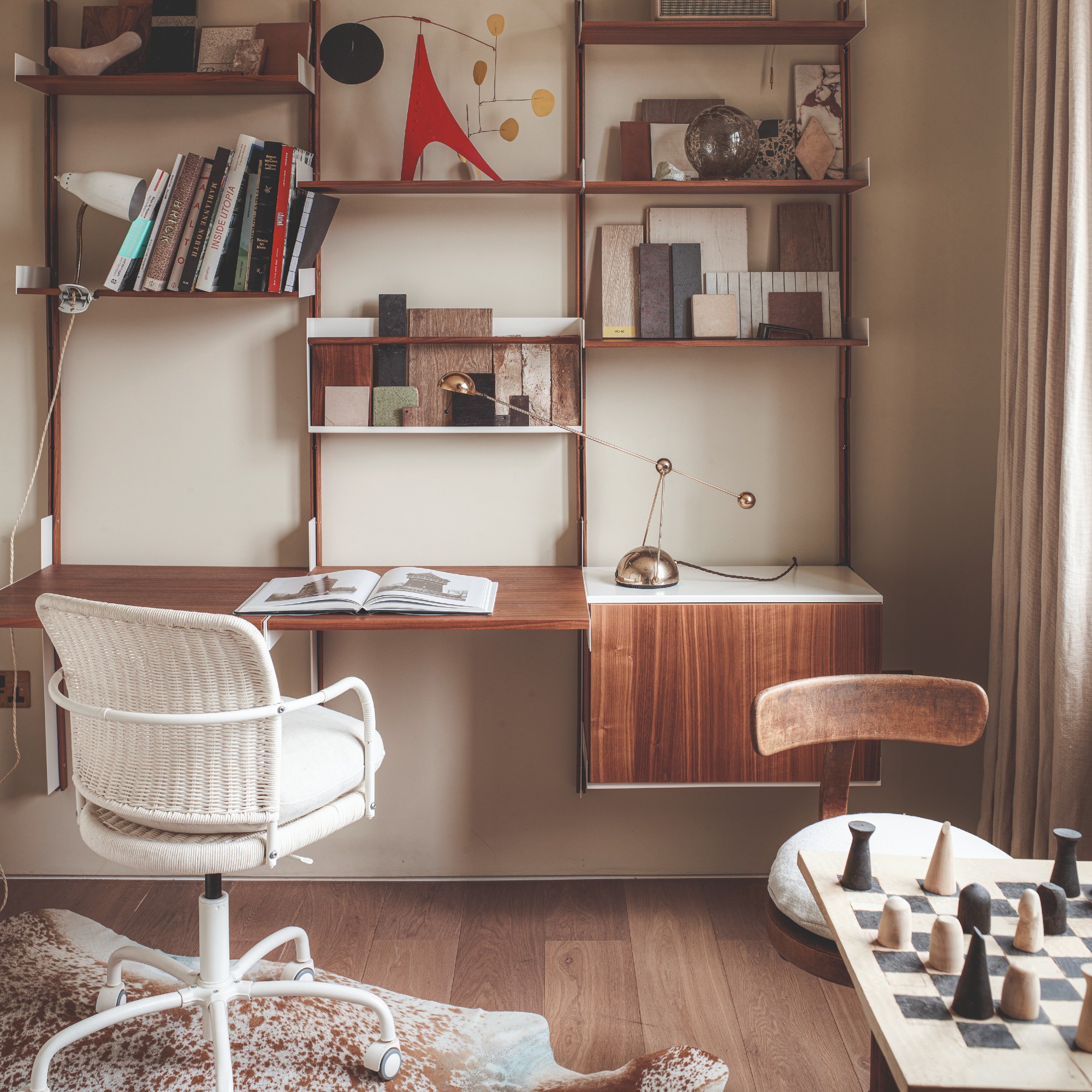 A home office with a wall-attached desk and shelving unit in a midcentury style with a table set with a modern chess set on the side