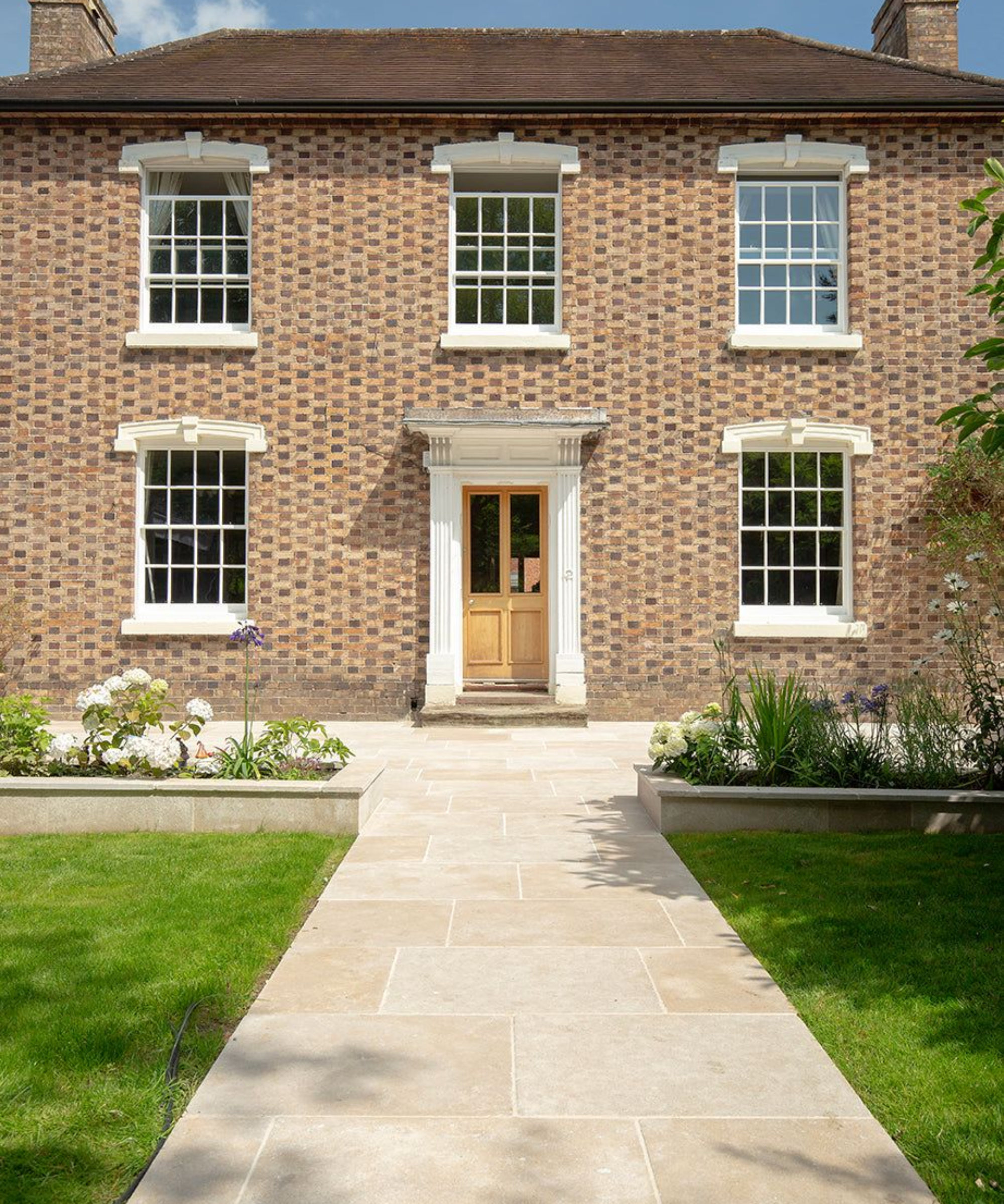 large double storey brick home with sash windows, yellow front door and path made of large beige tiles