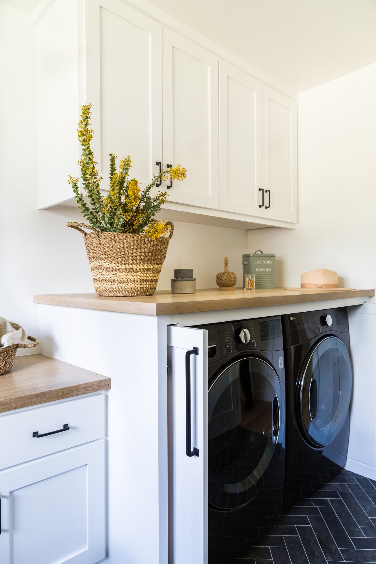 small laundry room ideas with appliances hidden behind cupboard doors. On the countertop is a basket with flowers inside it