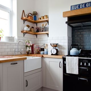 White kitchen with open corner shelving, Belfast sink and black range cooker