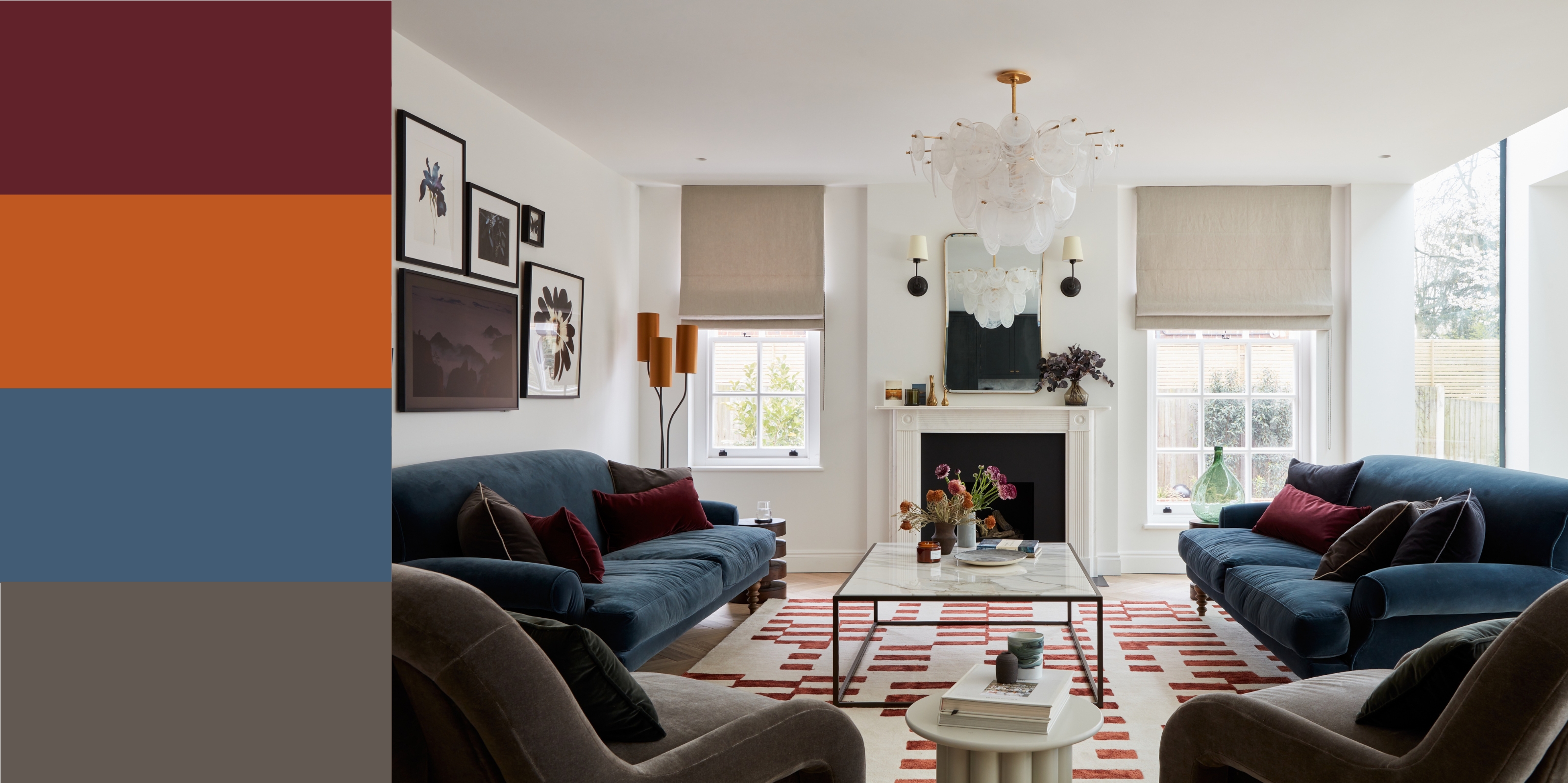 a living room with blue and gray sofas, burgundy pillows, and an orange lampshade. a patterned rug is on the floors, pictures on the wall, and gray blinds in the windows. 