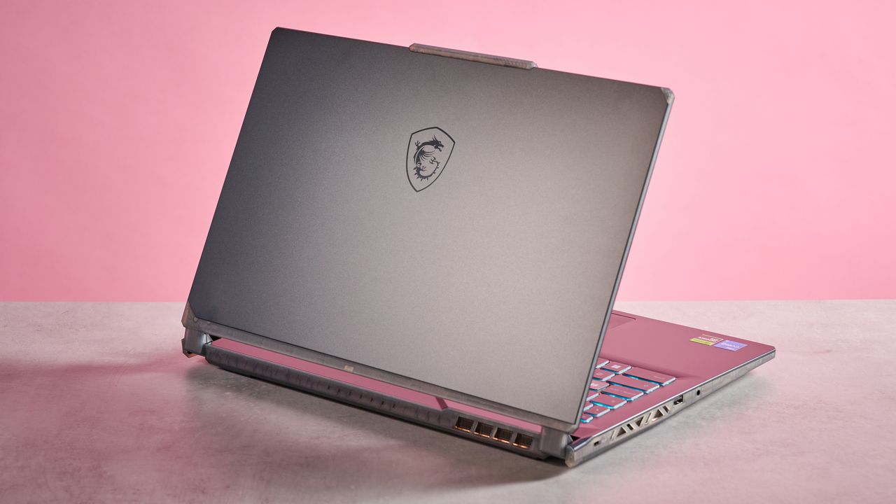Rear three-quarter view of MSI Cyborg 15 A13U open on desk on a pink background