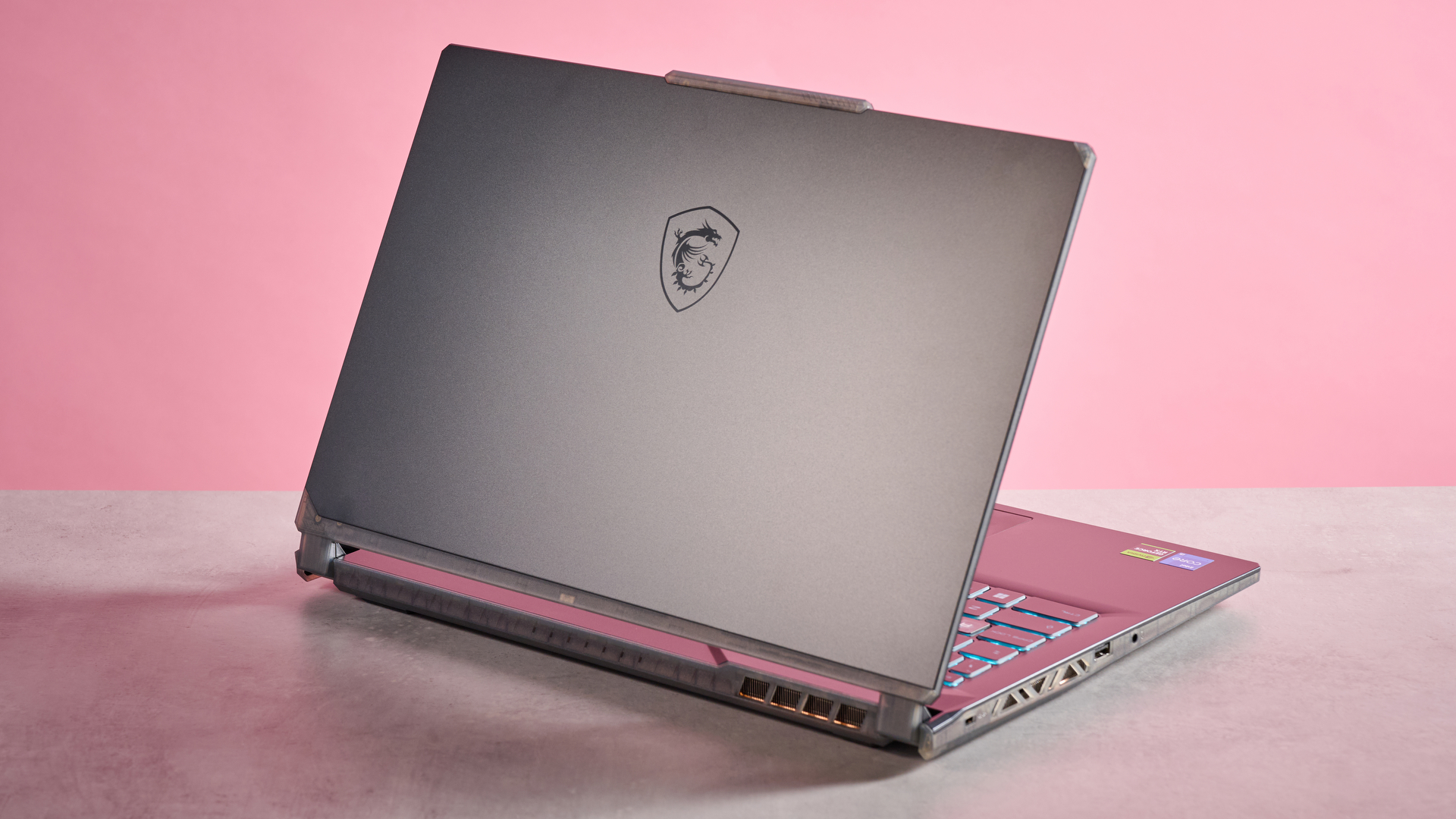Rear three-quarter view of MSI Cyborg 15 open on desk on a pink background