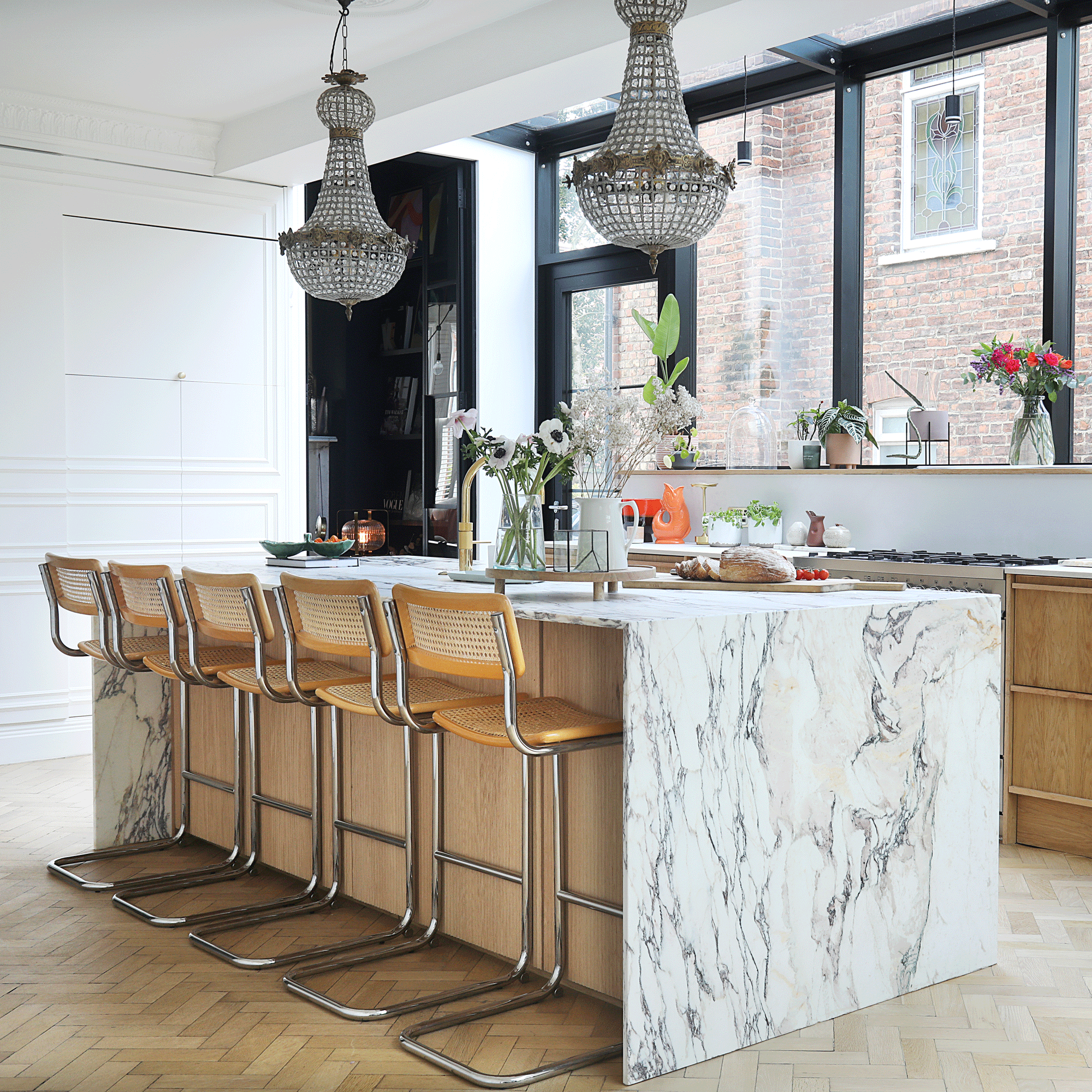 a neutral kitchen with a large kitchen island and five bar stools and two ornate chandeliers
